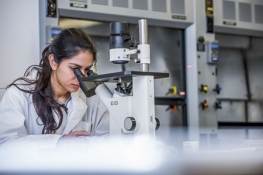 Female student with dark hair looking into a microscope